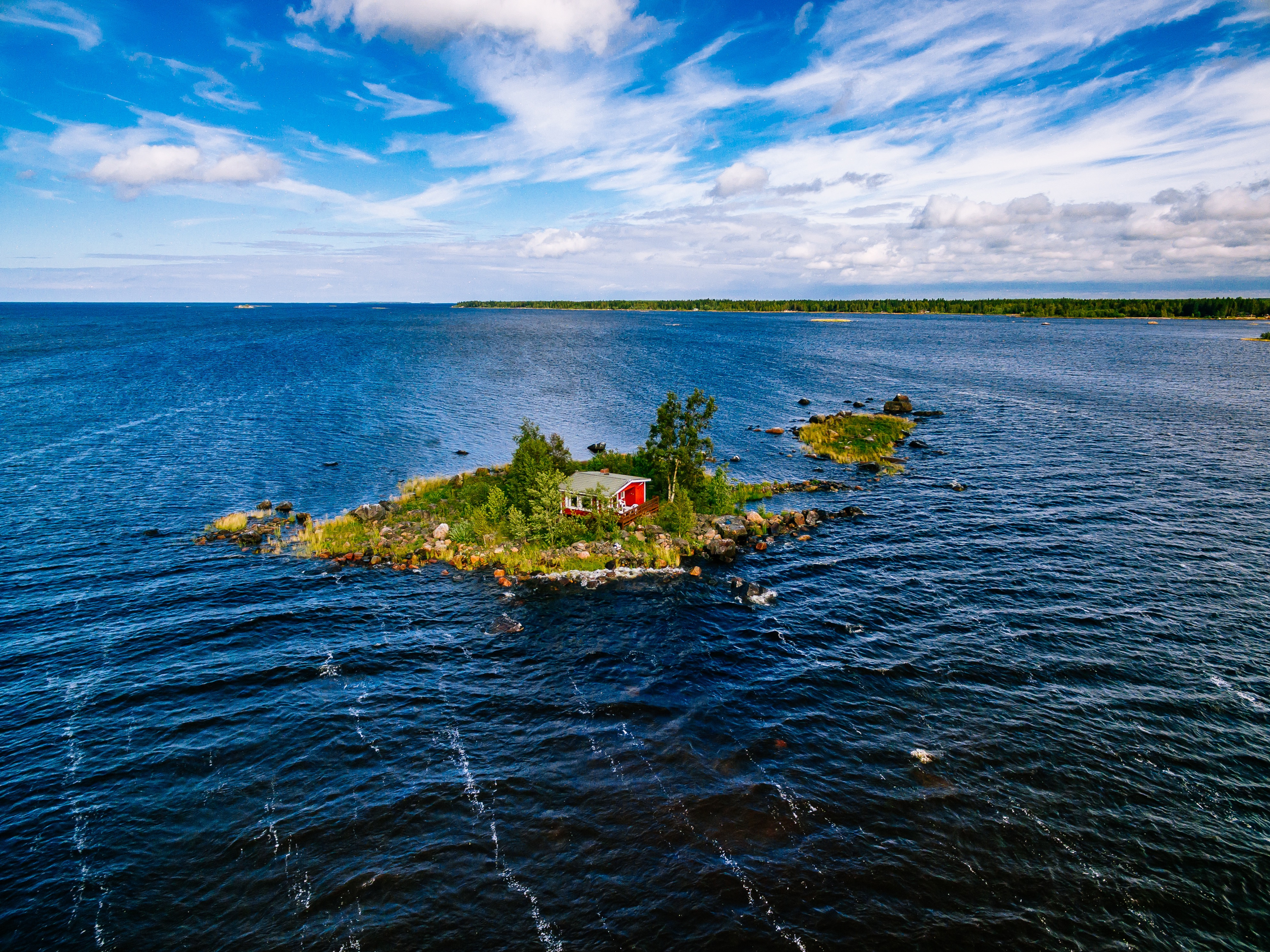 A small red cottage on an island in the blue sea on a summer day, Finland